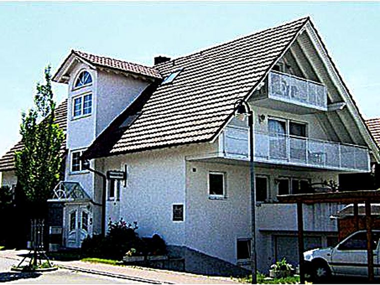 Das Haus der Pension Kuri: ein weißes Gebäude mit steilem Satteldach und Balkon an einem sonnigen Tag.